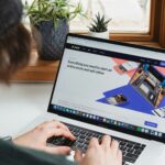 A person types on a laptop displaying the Shopify homepage.