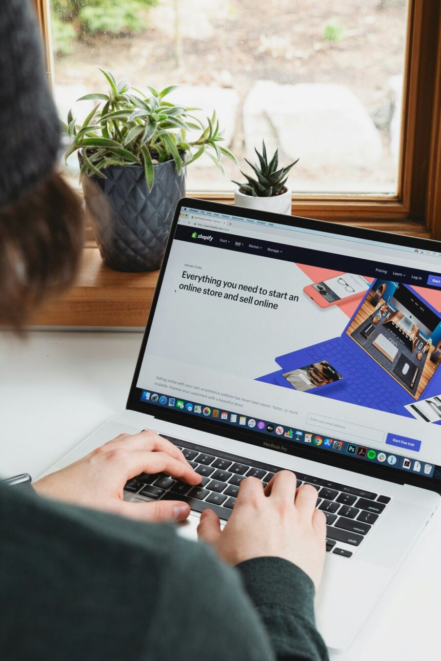 A person types on a laptop displaying the Shopify homepage.