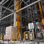 Automated warehouse with tall storage racks and a pallet of goods on a conveyor.