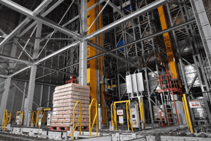 Automated warehouse with tall storage racks and a pallet of goods on a conveyor.