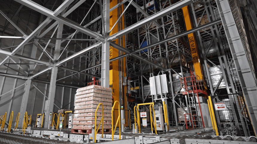 Automated warehouse with tall storage racks and a pallet of goods on a conveyor.