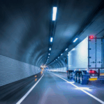 Semi-truck driving through a modern, brightly lit highway tunnel at night.