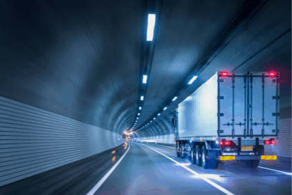 Semi-truck driving through a modern, brightly lit highway tunnel at night.