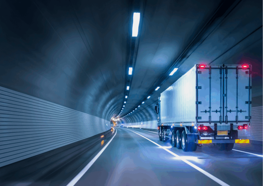 Semi-truck driving through a modern, brightly lit highway tunnel at night.