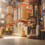 Warehouse workers in safety vests operating a forklift and managing inventory in a facility.