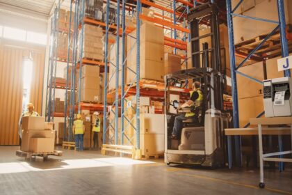 Warehouse workers in safety vests operating a forklift and managing inventory in a facility.