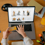Person shopping online on a laptop with a credit card at a desk.