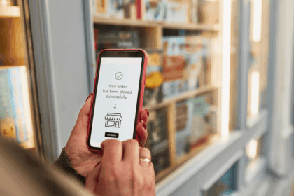 A person holds a smartphone displaying a successful order confirmation in front of a bookstore.