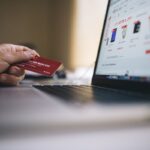 A person holding a loyalty card while shopping online on a laptop.