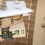 A person holding several Amazon packages in front of a front door.
