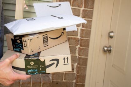 A person holding several Amazon packages in front of a front door.