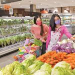 Two women wearing masks shopping for fresh produce in a grocery store.