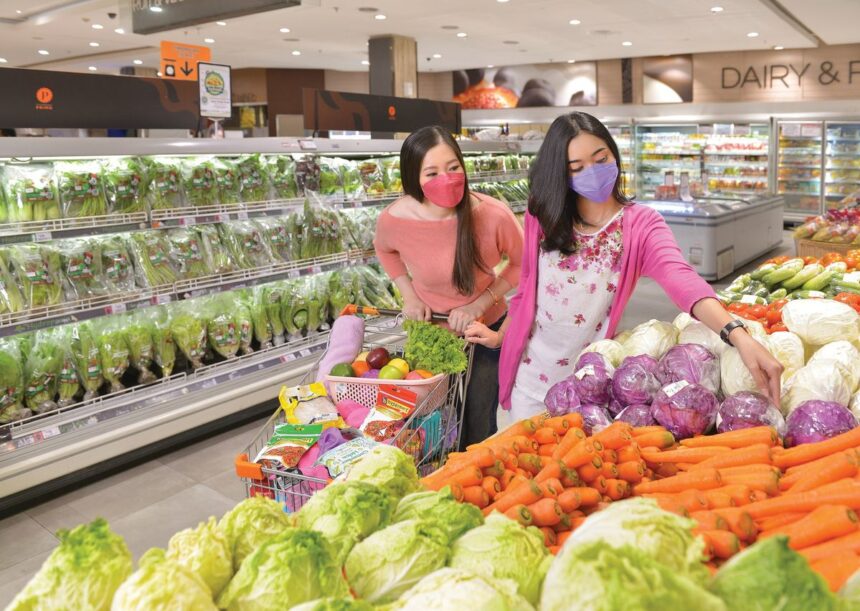 Two women wearing masks shopping for fresh produce in a grocery store.