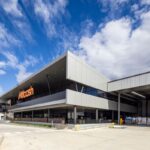 A modern, multi-story Metcash warehouse building under a blue, cloudy sky.