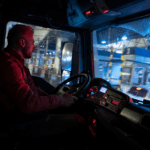 Truck driver sitting in the cab at a toll station at night.