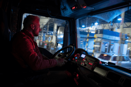 Truck driver sitting in the cab at a toll station at night.