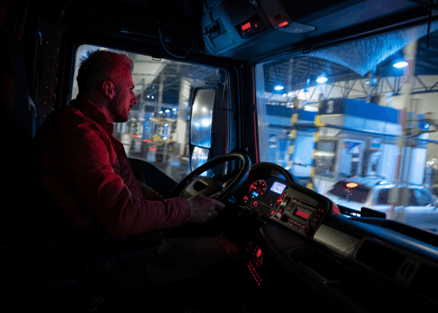 Truck driver sitting in the cab at a toll station at night.