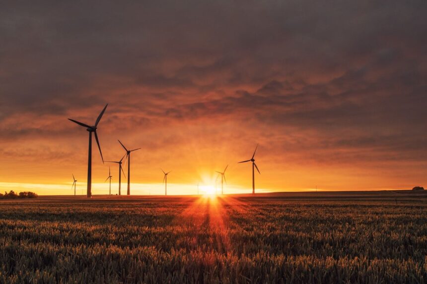 Wind turbines stand in a field during a vibrant, golden sunset.