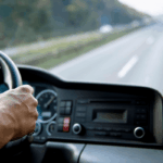 A driver's hand on a truck steering wheel, seen from the driver's perspective.