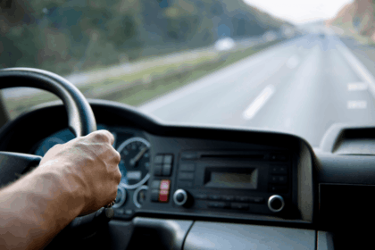 A driver's hand on a truck steering wheel, seen from the driver's perspective.