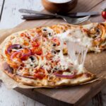 A slice of vegetable pizza with stringy melted cheese lifted from a wooden board.