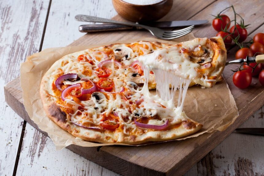 A slice of vegetable pizza with stringy melted cheese lifted from a wooden board.