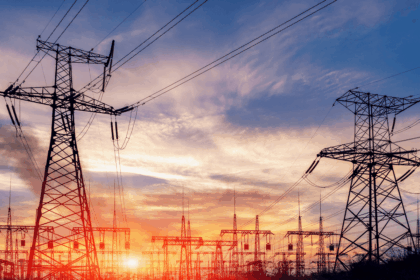 High-voltage power lines and electrical towers silhouetted against a vibrant sunset sky.