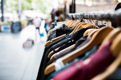 Clothes on wooden hangers hanging on a rack at an outdoor market.