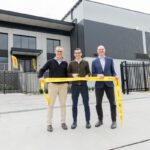 Three men cut a yellow DHL ribbon at a new warehouse opening.