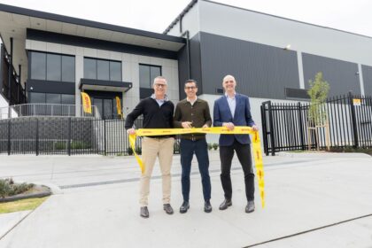 Three men cut a yellow DHL ribbon at a new warehouse opening.