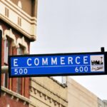 Street sign for E Commerce in San Antonio flanked by two green traffic lights.