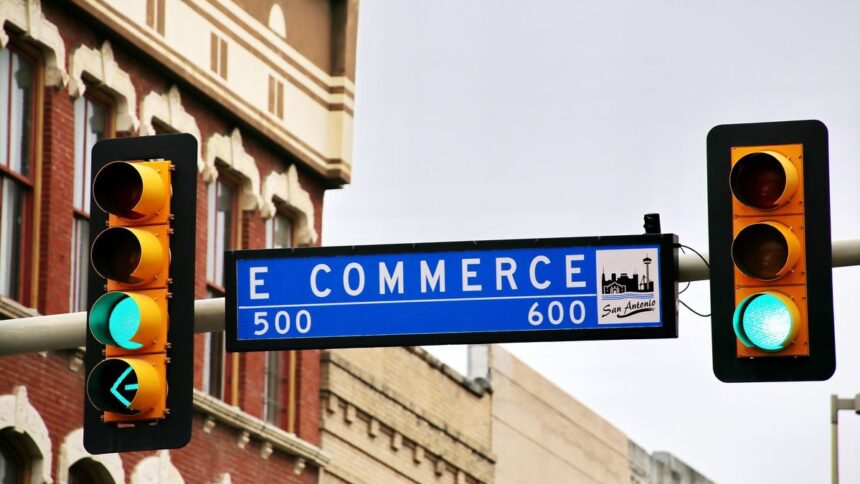 Street sign for E Commerce in San Antonio flanked by two green traffic lights.