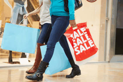 Two women walking through a mall carrying blue and red sale shopping bags.