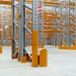 Empty warehouse featuring tall industrial metal shelving units with yellow protective guards.