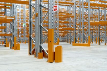Empty warehouse featuring tall industrial metal shelving units with yellow protective guards.