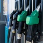 Close-up of several green-handled fuel pump nozzles at a gas station.