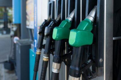 Close-up of several green-handled fuel pump nozzles at a gas station.