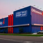 An Officeworks store exterior with a blue building, red accents, and sunset sky background.