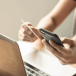 Person using a credit card and smartphone for online shopping near a laptop.