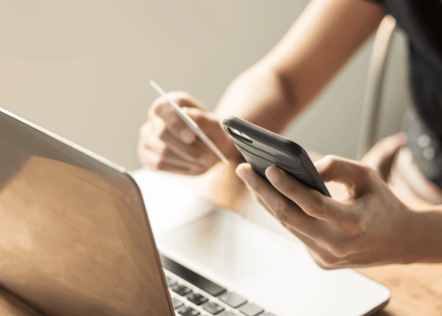 Person using a credit card and smartphone for online shopping near a laptop.