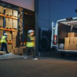 Workers in high-visibility vests loading boxes into a delivery van at a warehouse dock.