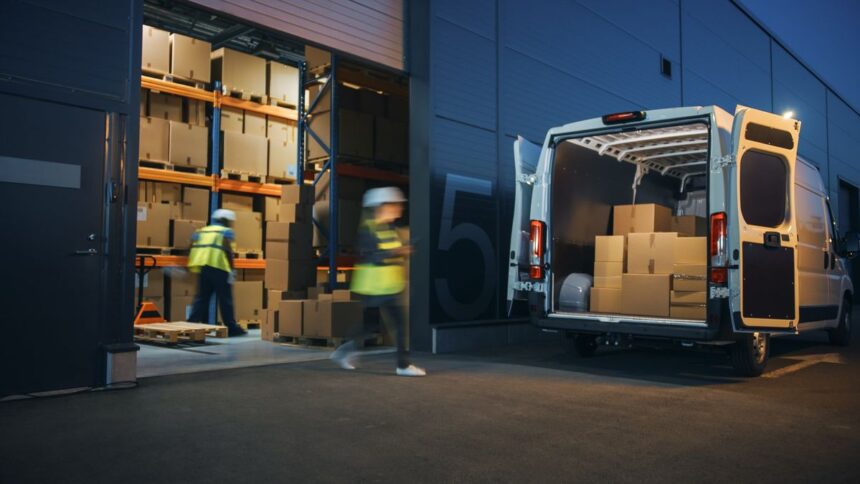 Workers in high-visibility vests loading boxes into a delivery van at a warehouse dock.