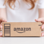 A person holding a brown cardboard Amazon package.