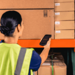 A warehouse worker in a high-visibility vest scans a cardboard box with a scanner.