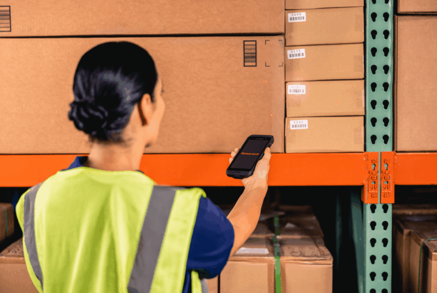 A warehouse worker in a high-visibility vest scans a cardboard box with a scanner.
