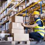 Warehouse worker in safety gear scanning cardboard boxes on a pallet.