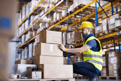 Warehouse worker in safety gear scanning cardboard boxes on a pallet.
