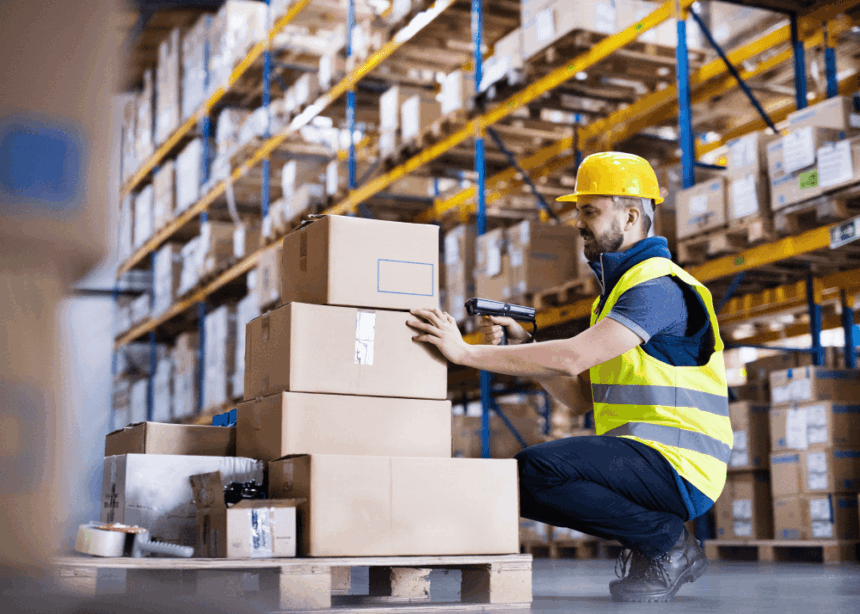 Warehouse worker in safety gear scanning cardboard boxes on a pallet.