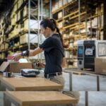 Warehouse worker processing shipping labels at a packing station.