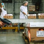 Hand holding a barcode scanner aimed at crates of produce in a warehouse.